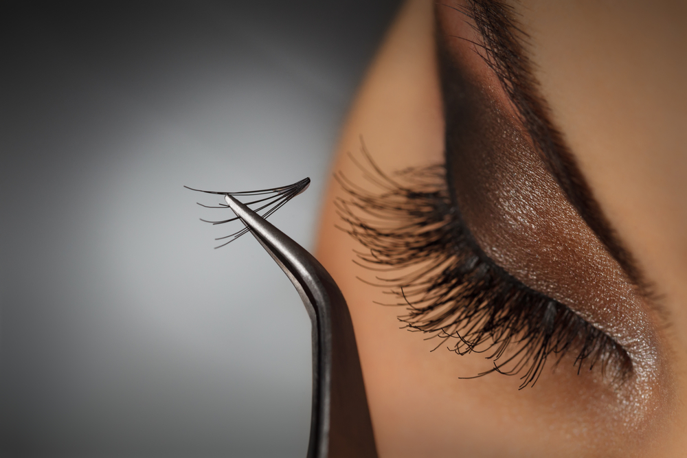 A woman having lash extensions applied with tweezers